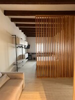 A modern hotel room with a wooden partition, a sofa, a desk with a computer, and a bed.