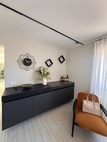 A modern living room with a black console table, a geometric clock, framed pictures, a vase with flowers, and a brown chair with a handbag.