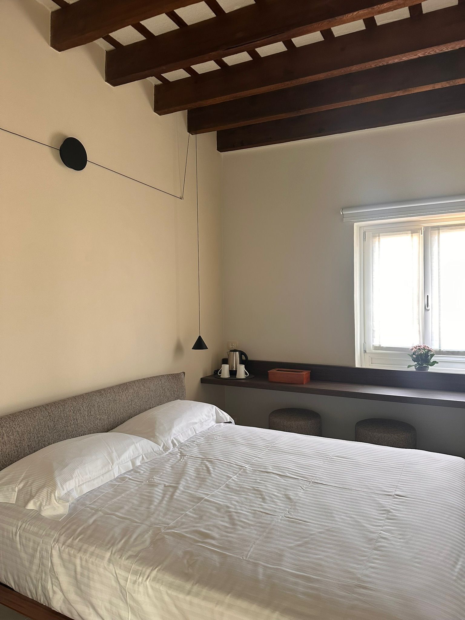 Een slaapkamer met een bed, een nachtkastje, een raam en een plafond met houten balken.