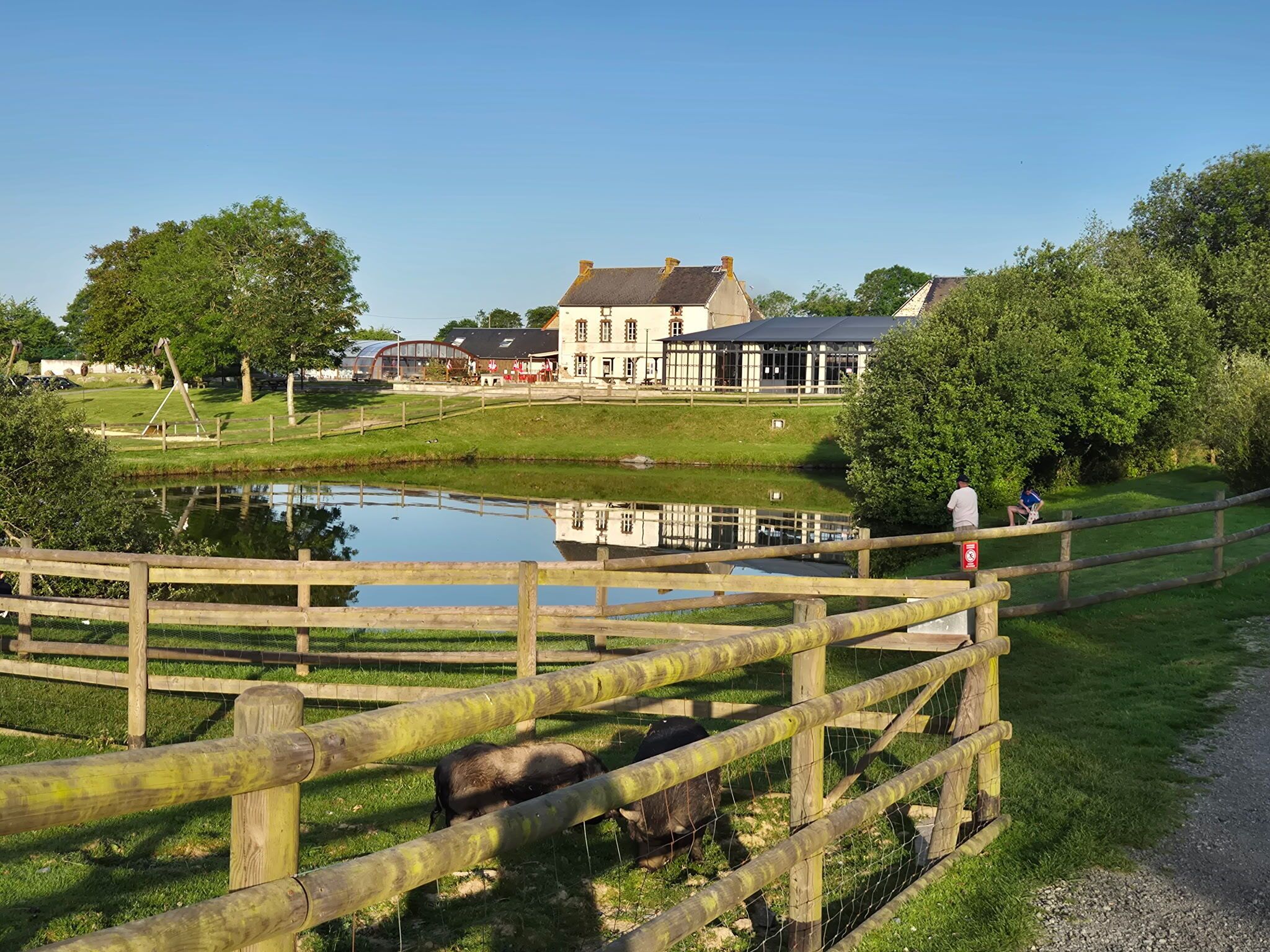 A wooden fence, a pond, and a building with a large window.