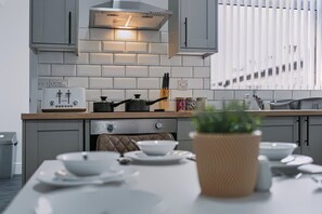 Eine moderne Küche mit weißen Schränken, einer Edelstahl-Dunstabzugshaube und einem Essbereich mit Tisch für zwei Personen.