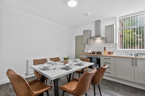 Eine moderne Küche mit Essbereich, mit einem weißen Tisch für vier Personen, grauen Schränken und einem Fenster mit Blick auf Grünflächen.