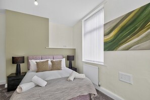 A bedroom with a bed, two bedside tables, a window with blinds, and a wall-mounted light fixture. - Stylish 2Bed, 2Bath Near Failsworth Manchester (Failsworth)