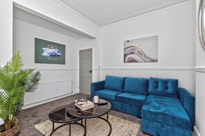 Ein Wohnzimmer mit einem blauen Sofa, einem Couchtisch mit Büchern, einer Pflanze und zwei Wandbildern.