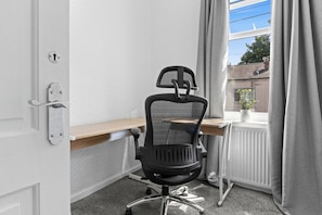 A room with a black office chair, a wooden desk, a white radiator, and a window with curtains. - Spacious 3BR Home | 15 Mins to Manchester (Swinton)