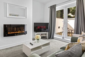 A modern living room with a flat-screen TV, a fireplace, and a sliding glass door to the outdoors. - Spacious 3BR Home | 15 Mins to Manchester (Swinton)