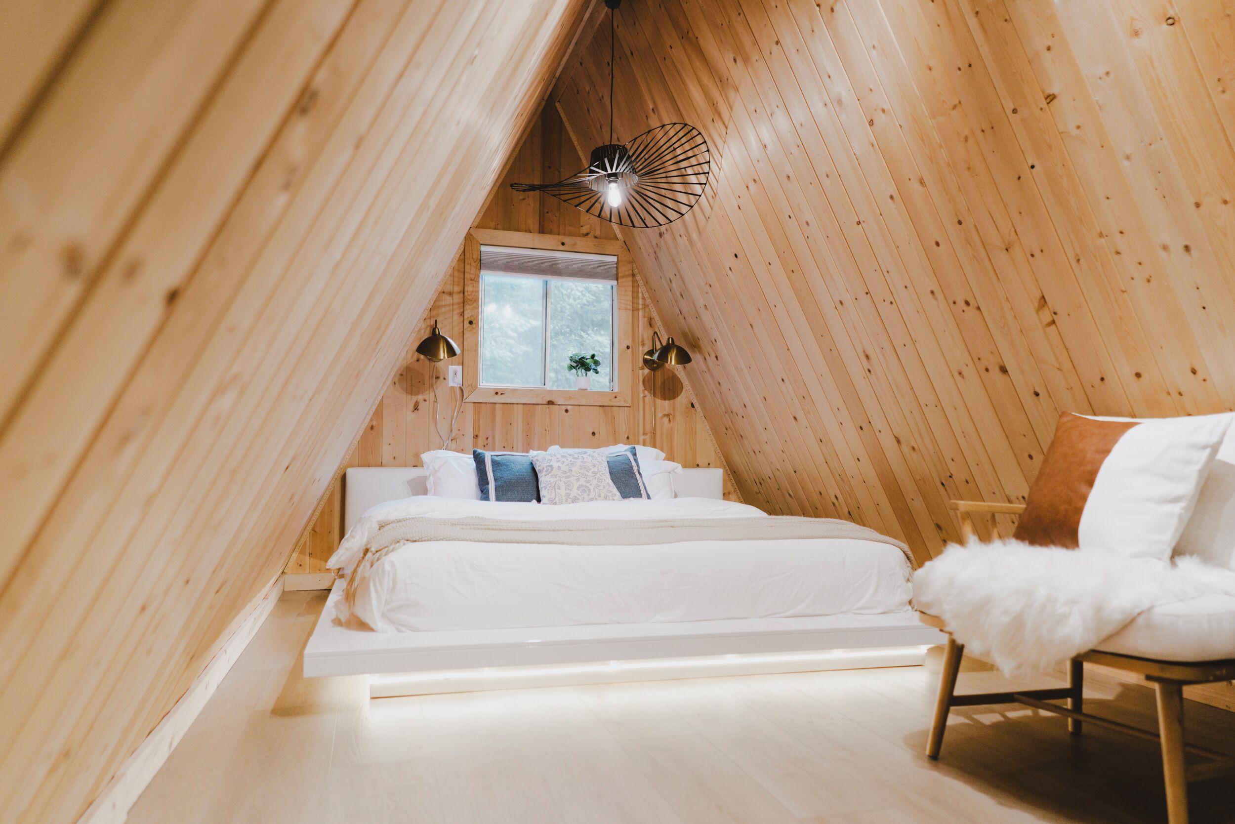 A cozy attic bedroom with a bed, a chair, a window, and a unique ceiling fan.