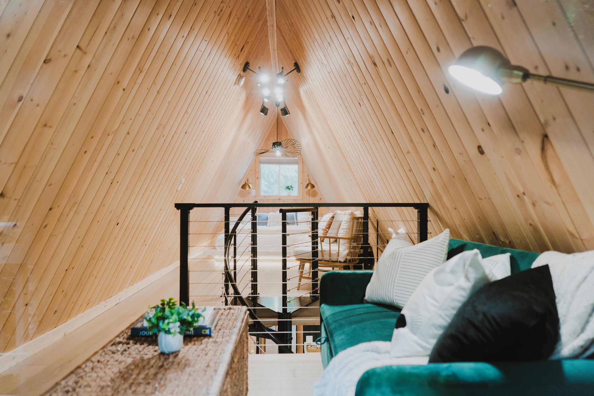 Ein gemütliches Interieur mit schrägverdeckter Decke, einem grünen Sofa, einem kleinen Tisch mit einer Pflanze und einer Treppe, die zu einer erhöhten Ebene führt.