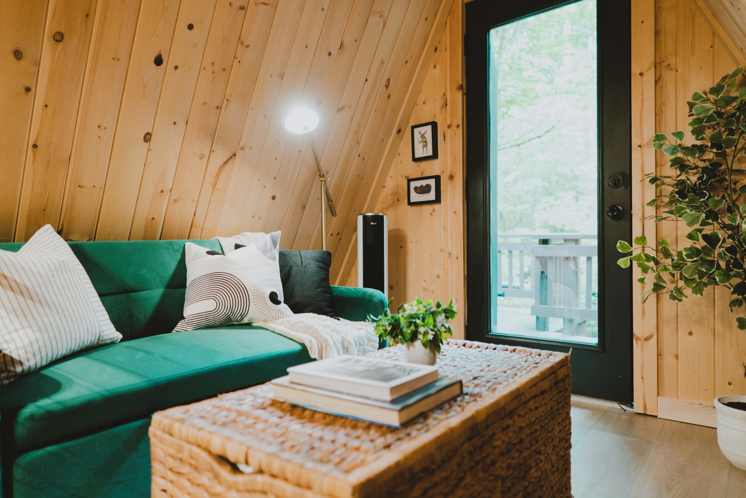 A cozy room with a green sofa, a woven coffee table, and a large window.