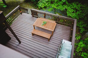 Una terraza de madera con una mesa y bancos, rodeada de follaje.