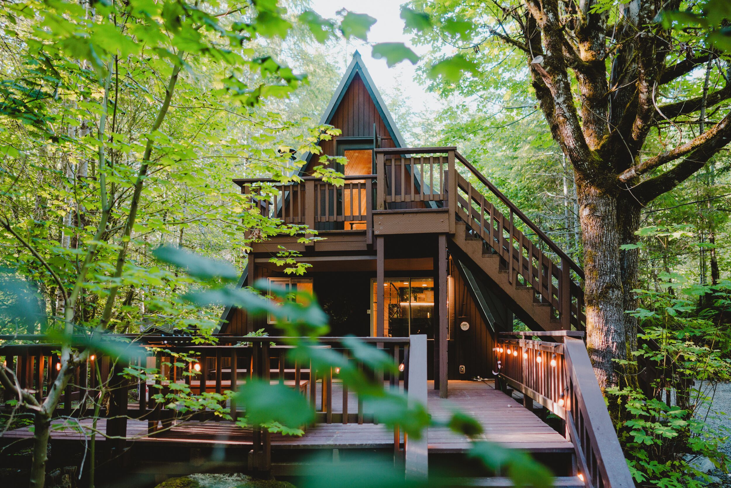 A cabin with a wooden deck, a staircase, and a view of the surrounding forest.