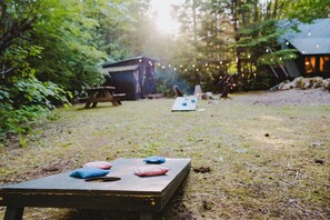 Juego de mesa de madera con cojines, una mesa de picnic y un cobertizo en un área boscosa.
