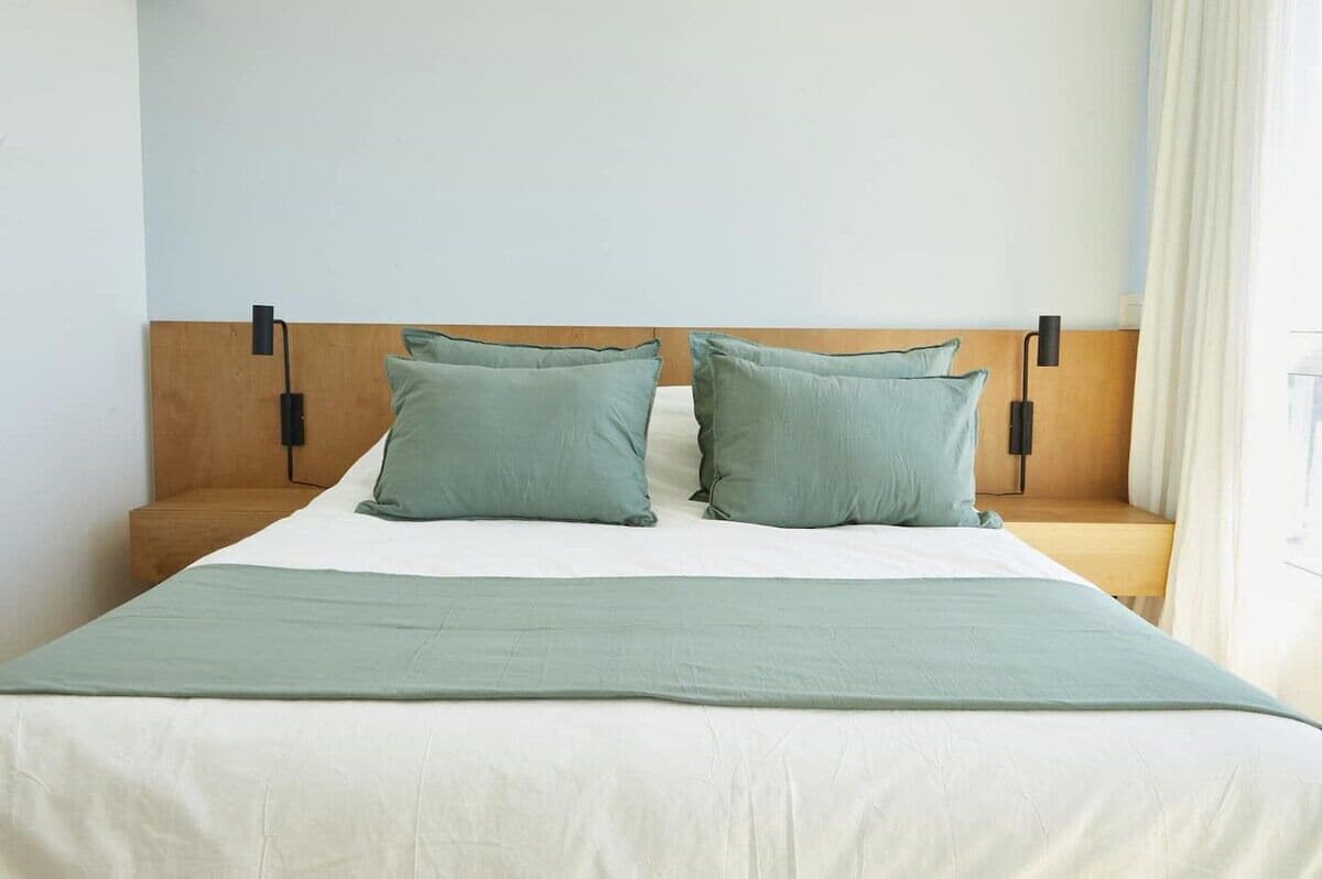 A bed with a wooden headboard, two pillows, a bedside table, and a lamp.