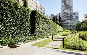 A landscaped pathway with a hedge, a bench, and a building in the background. - Hestia at Paraguay 4400 (Buenos Aires)