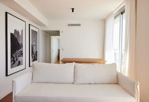 Una habitación minimalista con un sofá blanco, fotografías blanco y negro enmarcadas en la pared y un ventanal con cortinas de gasa.