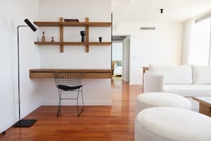 Ein moderner Wohnraum mit einer Holzhocheliege, einem schwarzen Drahtstuhl und einem weißen Sofa.