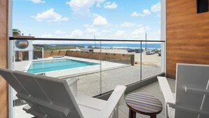 Un balcón con piscina, sillas de descanso y vista al mar.
