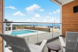 Een balkon met een zwembad, ligbedden en uitzicht op zee.