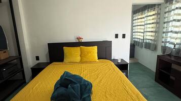Habitación de hotel con una cama grande, una mesita de noche y un ventanal con cortinas.