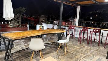 Una terraza en la azotea con una mesa de madera, dos sillas y una barandilla con vistas a la ciudad de noche.