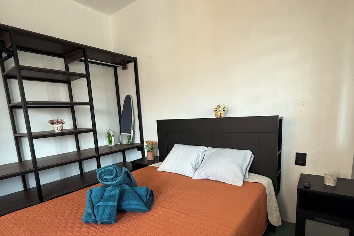 Ein Hotelzimmer mit einem Bett, einem Nachttisch, einem Regal und einem an der Wand befestigten Spiegel.