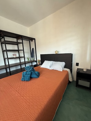 Ein Hotelzimmer mit einem Bett, einem Nachttisch, einem Regal und einem an der Wand befestigten Spiegel.