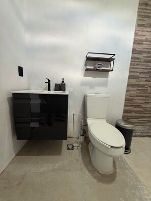 Ein modernes Badezimmer mit einer weißen Toilette, einem schwarzen Waschtisch und einem kleinen Regal über der Toilette.