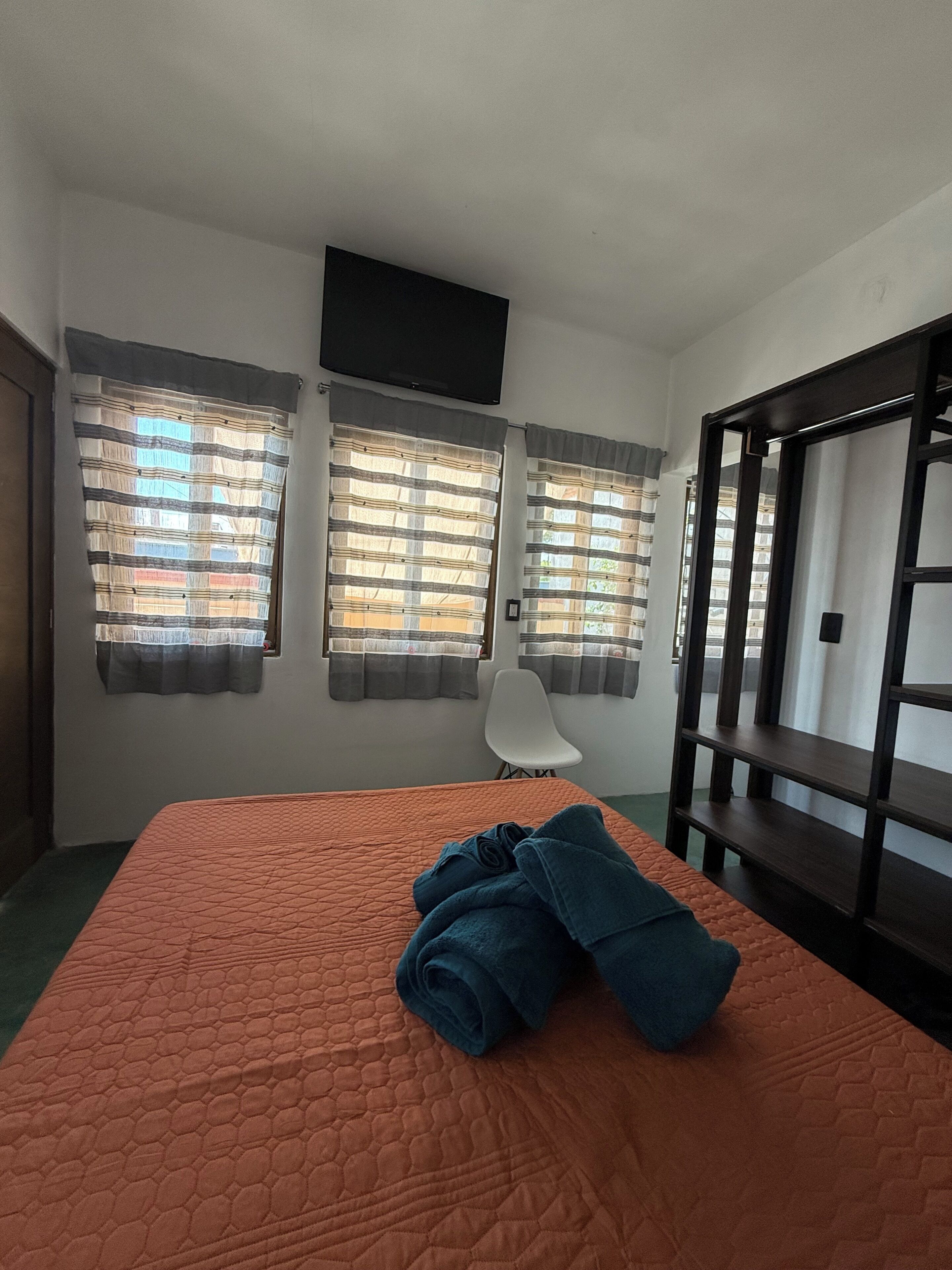 Una habitación con una cama, una silla y un televisor montado en la pared.