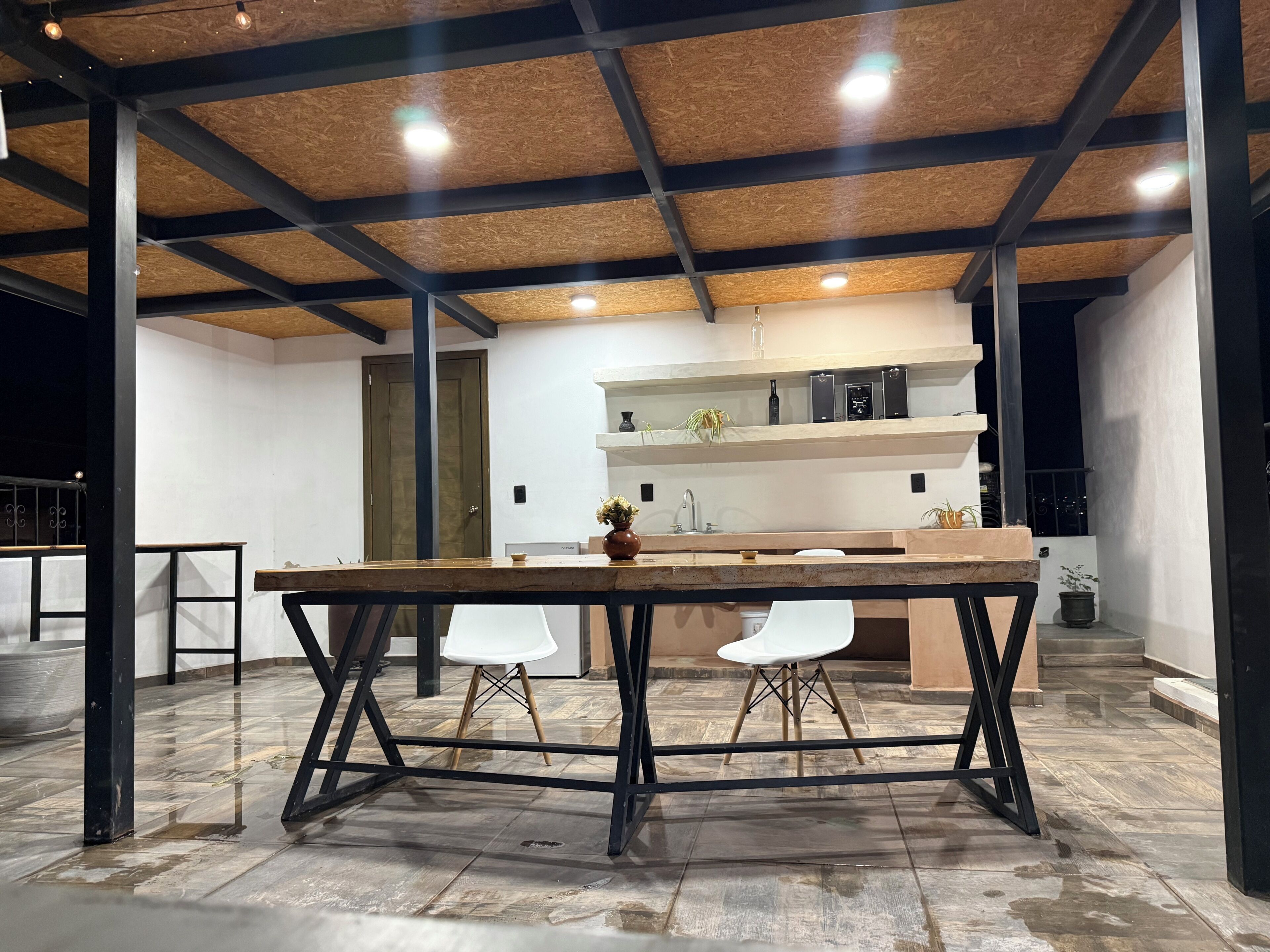 Una cocina moderna con encimera de madera, taburetes, una silla blanca y un mueble estante empotrado.