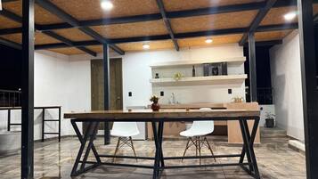 Una cocina moderna con encimera de madera, taburetes, una silla blanca y un mueble estante empotrado.