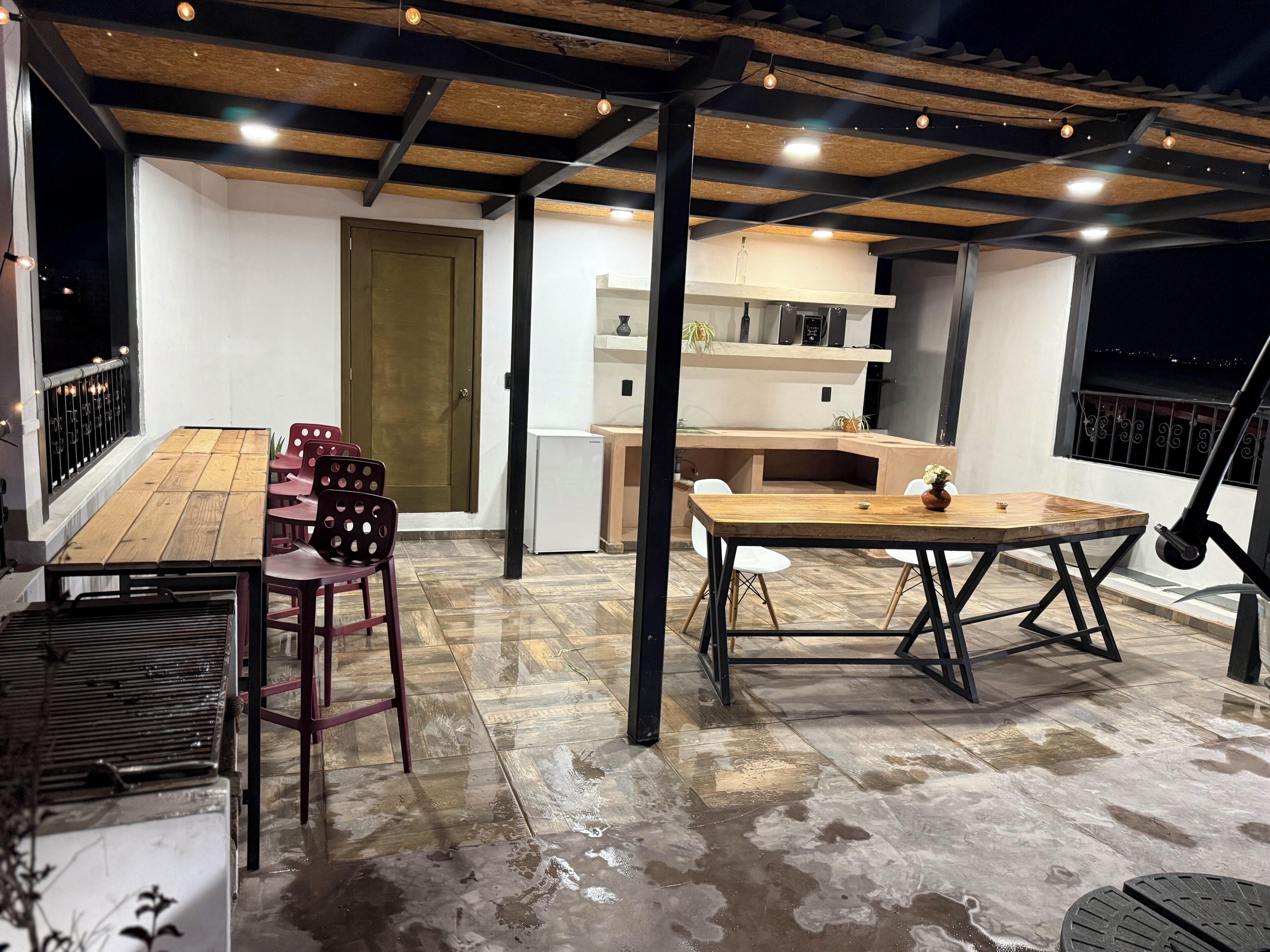 Un patio al aire libre con una mesa y sillas de madera, un refrigerador blanco y una puerta de madera.