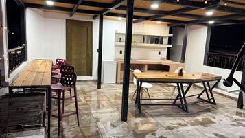 Un patio al aire libre con una mesa y sillas de madera, un refrigerador blanco y una puerta de madera.