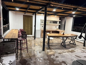 Ein Außenbereich mit einer Terrasse, einem Holztisch und Stühlen, einem weißen Kühlschrank und einer Holztür.
