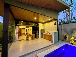 Cozinha moderna com armários de madeira, área de jantar com mesa e cadeiras, e área de piscina com borda iluminada em azul.