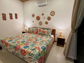 A bedroom with a floral-patterned bedspread, a wooden headboard, two bedside lamps, and decorative wall art. - Awesome 4-bedroom estate with AC in charming Puerto Viejo (Puerto Viejo)