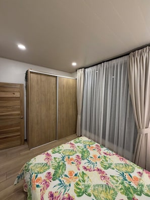 Quarto com cama, guarda-roupa de madeira e janela com cortinas.