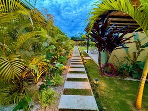 Un sentier de jardin agrémenté de plantes tropicales et surmonté d’une pergola.