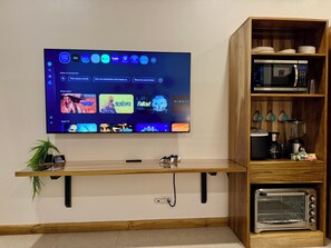 Un téléviseur à écran plat fixé au mur, avec une étagère en bois en dessous où sont exposés des appareils de cuisine.