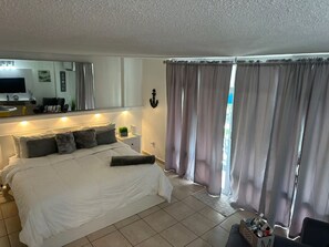 Una camera d'albergo con un letto, un comodino, una lampada, tende e vista sull'esterno.