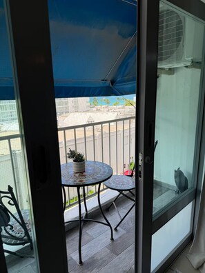 Ein Balkon mit Tisch und Stühlen, einer Topfpflanze und Blick auf ein Gebäude und Palmen.