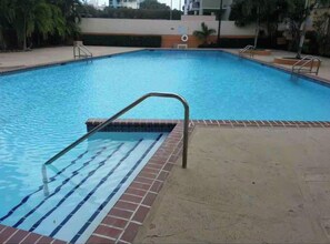 Ein Schwimmbecken mit einer gefliesten Terrasse und Metallgeländern.