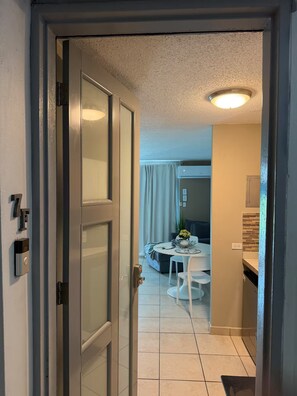 Ein Hotelzimmer mit einer Schiebetür, einem Bett, einem Nachttisch, einem kleinen Tisch mit Stühlen und einer Deckenleuchte.