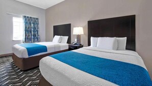 Ein Hotelzimmer mit zwei Betten, einem Fenster mit gemusterten Vorhängen, einem Nachttisch mit Lampe und einem Teppich mit Muster.