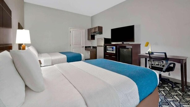 Ein Hotelzimmer mit zwei Betten, einem Schreibtisch mit Stuhl, einem Fernseher und einer Küchenzeile.