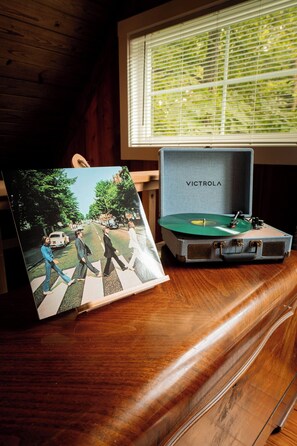 A vinyl record player in a blue case with the brand name 'VICTROLA' on it, placed on a wooden surface near a window with blinds.