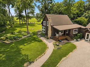 A two-story house with a stone chimney, a front porch with seating, and a well-maintained lawn.