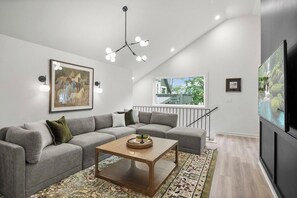 Een moderne woonkamer met een hoekbank, een salontafel, een kroonluchter en kunstwerken aan de wanden.