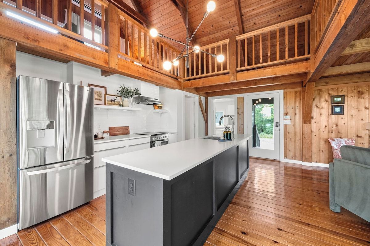 A modern kitchen with a large island, stainless steel appliances, and wooden beams.