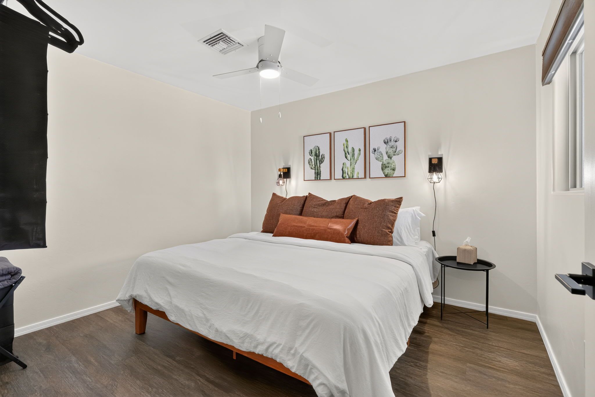 Une chambre à coucher comprenant un lit, une table de chevet, une lampe fixée au mur et un ventilateur de plafond.