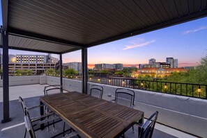 A covered outdoor seating area with a table and chairs, overlooking a cityscape with modern buildings. - Presidio Flat at Hoff & Co | Downtown Tucson (Tucson)